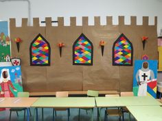 a classroom with tables, chairs and paintings on the wall in front of them that have stained glass windows