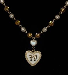 The piece combines 6mm beads: clear with golden sparkles and white pearlescent, alternating for a delicate shimmer. At it's heart lies a heart shaped pearlescent bead, with a dainty heart shaped pendant handing below, adorned with a gold bow framed by tiny pearls. All the beads are connected with a gold toned wire and incudes an extension chain for adjustable length, secured with a lobster claw clamp. Heart Shaped Pendant, Heart Shape Pendant, A Heart, Halloween Shopping, Heart Shapes, Gold Tones, Beaded Necklace, Jewelry Necklaces, Accessory Gift