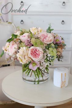 a vase filled with pink and white flowers sitting on top of a table next to a roll of toilet paper