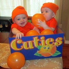 two babies are sitting in a box with balloons and an orange sign that says cuties