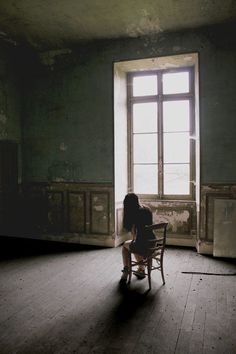 a woman sitting on a chair in an empty room next to a window with sunlight coming through the window