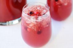 two glasses filled with liquid sitting on top of a white table next to red apples