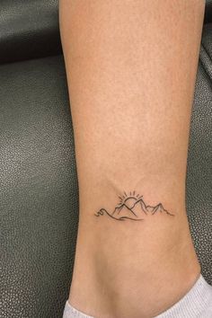 a woman's foot with a small tattoo on the side of her leg, and mountains in the background