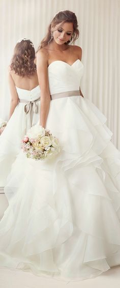 two women in white dresses standing next to each other with bouquets on their laps