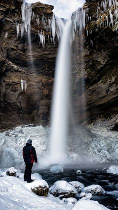 a person standing in front of a waterfall with icicles hanging from it's sides