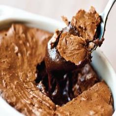 a spoon full of chocolate ice cream on top of a white bowl filled with pudding