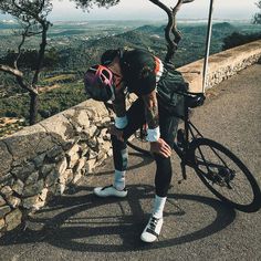 a man on a bike leaning against a stone wall and looking down at the ground