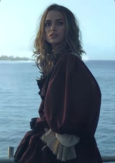 a woman standing on top of a boat next to the ocean and looking at the camera