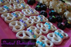 there are many pretzel butterflies on the pink tray with blue and white candies