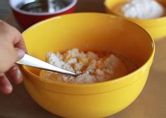 a person is spooning sugar into a yellow bowl