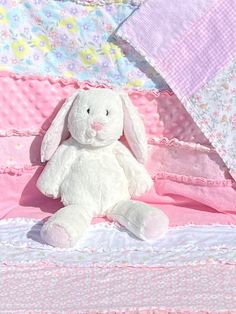 a white stuffed rabbit sitting on top of a pink and white bedding with flowers