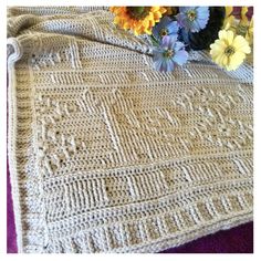 a crocheted blanket sitting on top of a table next to flowers