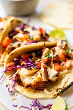 three fish tacos with slaw, coleslaw, and lime wedges