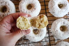 a hand holding a half eaten doughnut in front of other donuts on a cooling rack