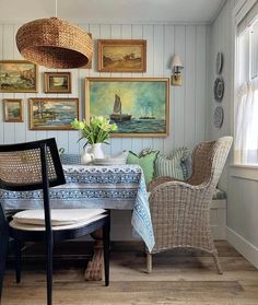 a dining room table with chairs and pictures on the wall above it, along with two wicker chairs