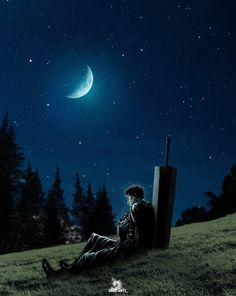 a man sitting in the grass looking up at the night sky with a half moon above him