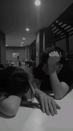 two people sitting at a table with their arms around each other's head and one person covering their eyes