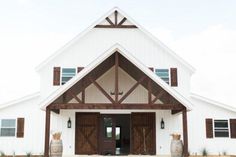 a large white building with wooden doors and two barrels in front of the entrance to it