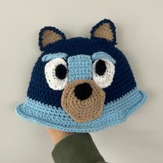 a crocheted bear hat is held up to the camera by someone's hand