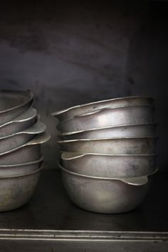 a stack of silver bowls sitting on top of a metal shelf next to each other