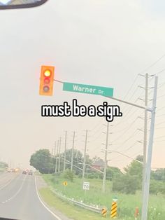 a street sign that says must be a sign on the side of the road in front of a traffic light