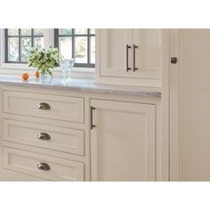 a kitchen with white cabinetry and marble counter tops, along with a vase filled with flowers