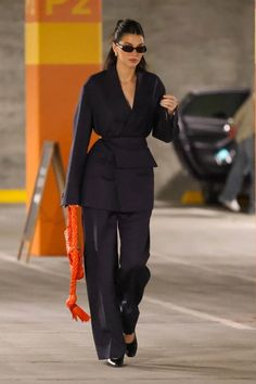 a woman walking down the street in a black suit and orange scarf on her head