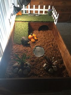 a wooden box filled with grass and rocks next to a white picket fence on top of a carpeted floor