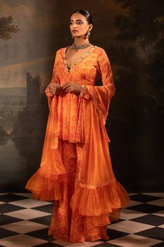 Tangerine peplum kurta with floral print and mirror, thread, pearl, bead, gota embroidered neckline. Paired with gharara and dupatta.
Components: 3
Pattern: Printed, Embroidery
Type Of Work: Floral, mirror, thread, pearl, bead, gota
Neckline: Plunge V neck
Sleeve Type: Full sleeves
Fabric: Georgette, Organza, Lining: Crepe
Color: Orange
Other Details: 
Length:
Kurta: 34 inches
Gharara: 42 inches
Sheer dupatta
Pleated frill hem
Occasion: Sangeet - Aza Fashions V Neck Kurta, Sheer Dupatta, Printed Embroidery, Floral Mirror, Embroidered Neckline, Full Sleeves, Set For Women, Aza Fashion, Fashion Set