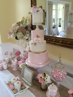 a table topped with a pink and white cake next to other desserts on top of it