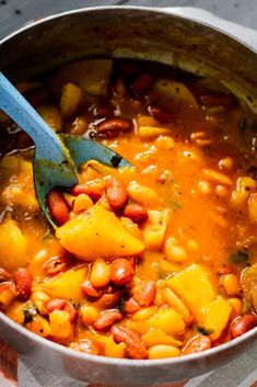 a pot filled with beans and vegetables on top of a tablecloth next to a spoon