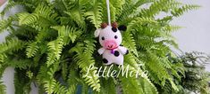 a crocheted cow hanging from a fern plant