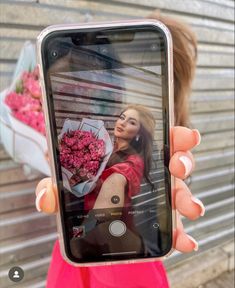 a woman taking a selfie with her cell phone in front of a bunch of flowers