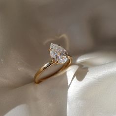 a gold ring with a pear shaped diamond on it's side sitting on a white cloth