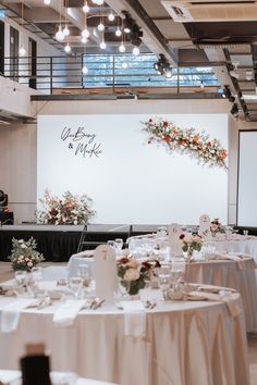 a banquet hall with tables and chairs set up for a formal function, decorated with flowers and greenery