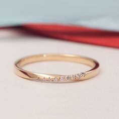 a gold wedding band with five diamonds on it sitting on a white surface next to a red bag