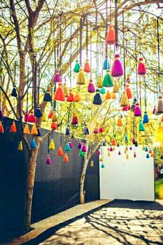 a tree with many colorful tassels hanging from it's branches in front of a fence