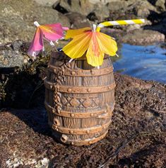 two paper flowers are placed in a vase on the rocks by the water's edge