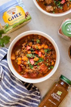 two bowls filled with chili and beans next to a jar of gheee seasoning