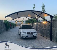 a white car is parked in front of a stone wall with an awning over it