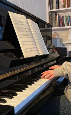 a person sitting at a piano with their hands on the keyboard and music books behind them