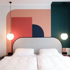 a bed with white sheets and pillows in front of a colorful wall