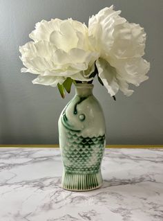 a green vase with white flowers in it on a marble countertop next to a gray wall