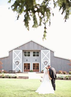 a bride and groom kissing in front of a barn at the end of their wedding day