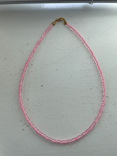 a pink beaded necklace hanging from a hook on a white wall with a gold plated clasp