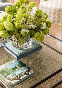 a glass table topped with books and a vase filled with flowers on top of it