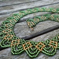 a green and gold beaded necklace sitting on top of a wooden table