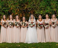 a group of women standing next to each other in front of trees and bushes holding bouquets