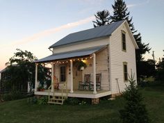 a small white house with porches and rocking chairs on the front porch at dusk