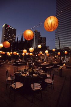 an outdoor dining area with paper lanterns hanging from the ceiling and tables set for dinner